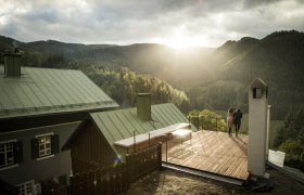 Villa Antoinette, © Matthias Kronfuss Zwei Personen stehen auf einer Terrasse mit Blick auf bewaldete Berge bei Sonnenuntergang.