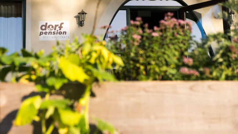 Eingang, © Dorfschmiede eG Eingang der Dorfpension Mariahilfberg mit Pflanzen im Vordergrund.