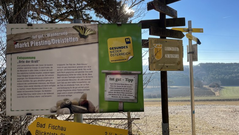 Blickplatz Rotes Kreuz, © Wiener Alpen/Katharina Lechner Wegweiser und Informationstafel in einer ländlichen Landschaft mit blauem Himmel.