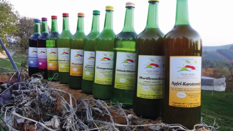 Fruit juices from the Winkler family, © Familie Winkler A row of different fruit juice bottles on a wooden beam outside.