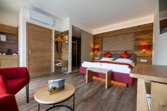 The guest house in the Triad, © Marketing Platzhirsch, Gobauer Modern guest room with double bed, wooden furniture and red accents.