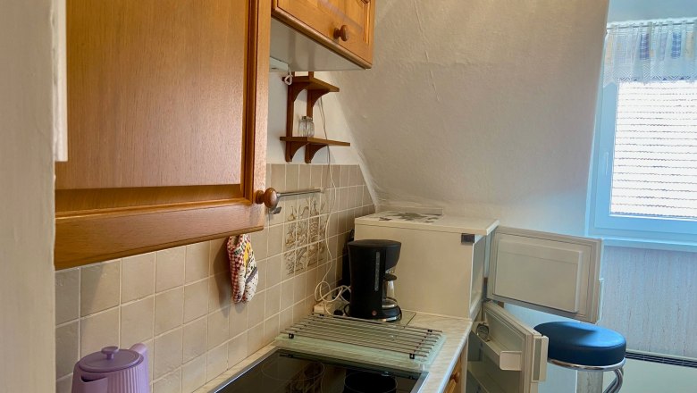 Küche (c)wieneralpen, © Wiener Alpen Kleine Küche mit Holzschränken, Herd, Kaffeemaschine und offenem Kühlschrank.