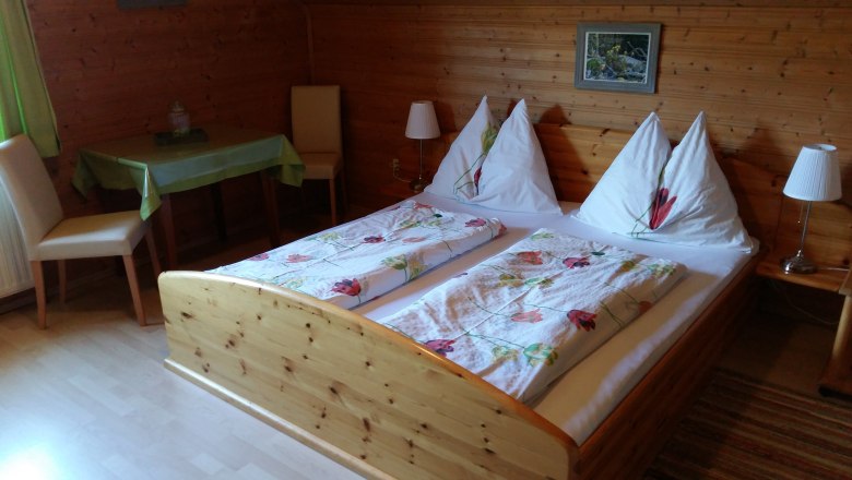 Zimmer im Bauernhof Wachabauer, © Wachabauer Gemütliches Zimmer mit Holzwänden, Doppelbett und Tisch im Bauernhof Wachabauer.