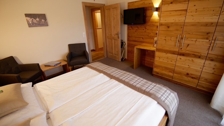 Große Ferienwohnung, © rosinger Schlafzimmer mit Doppelbett, Holzmöbeln und Fernseher an der Wand.