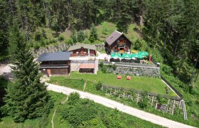 Pottschacherhütte, © Georg Eder Luftaufnahme der Potschacherhütte in einem Waldgebiet mit umliegenden Bäumen und einer Terrasse mit Sonnenschirmen.