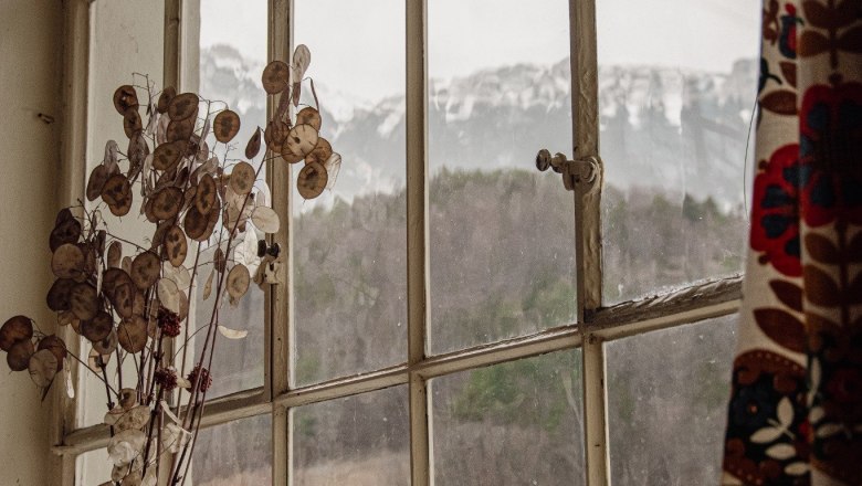 Orlet an der Rax, © Sofia Orlet Blick aus einem Fenster mit Berglandschaft im Hintergrund, Vase mit Trockenblumen im Vordergrund.