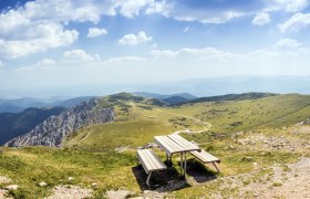 Blickplatz Fischerhütte Schneeberg, © Wiener Alpen, Foto: Franz Zwickl Panoramablick von einem Berg mit einer Bank im Vordergrund und grünen Hügeln im Hintergrund.