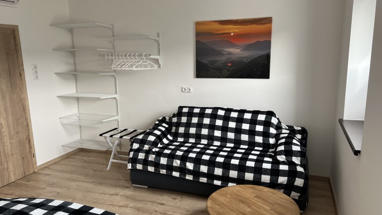 Schalfzimmer, © Anton Sommer Schlafzimmer mit kariertem Sofa, Wandregal und Landschaftsbild.