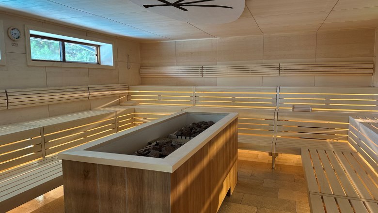 Zen-Sauna Linsberg Asia, © Linbsberg Asia Innenansicht einer modernen Sauna mit Holzbänken und einem Ofen in der Mitte.