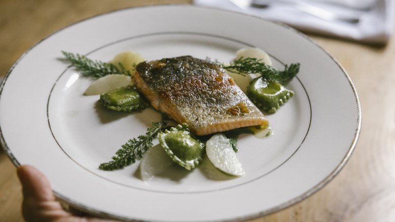 Kräuterwirtin Gerda Stocker Lachsforellenfilet mit Brennnesseltascherl und weißen Rüben, © Wiener Alpen/Sophie Menegaldo Ein Teller mit Lachsforellenfilet, Brennnesseltascherl und weißen Rüben, dekoriert mit Kräutern.