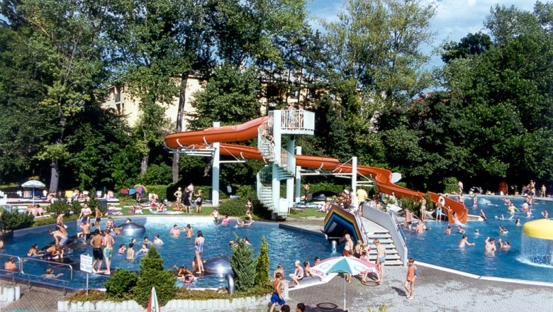 Blub Parkbad Ternitz, © Stadtgemeinde Ternitz Ein Freibad mit vielen Menschen, einer Wasserrutsche und Bäumen im Hintergrund.