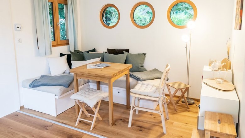 Sitzbereich Luna, © WW Wohnwagon GmbH Gemütlicher Sitzbereich mit Holztisch, Stühlen und runden Fenstern.