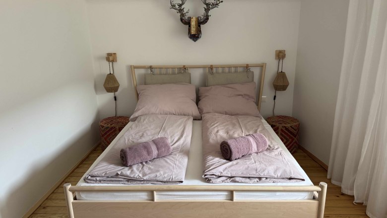 Room view in Dottore Casa, © Michael Liska Bedroom with double bed, pink bed linen and towels, wooden floor and wall decoration.