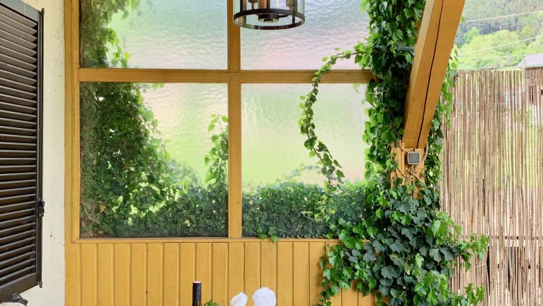 Top 1 - Terrasse, © VP FeWo OG Ein gedeckter Tisch auf einer Terrasse mit Weinflasche, Geschirr und Kerzen, umgeben von Efeu und Holzwänden.