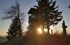Aussichtswarte Gschaidt, © Wiener Alpen Sonnenuntergang hinter einem Aussichtsturm und Bäumen.