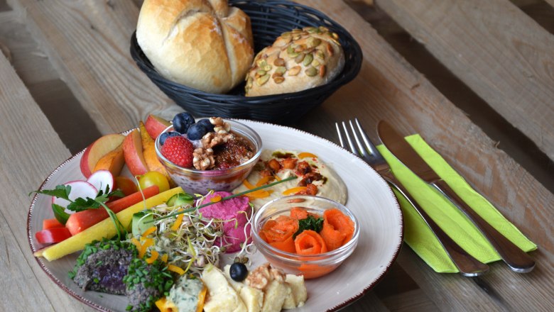 Schlemmen im Turmcafé, © dasTurmcafé - Gemeinde Schwarzenbach Bunter Frühstücksteller mit Hummus, Käse und Gemüse, daneben Besteck und ein Brotkorb.