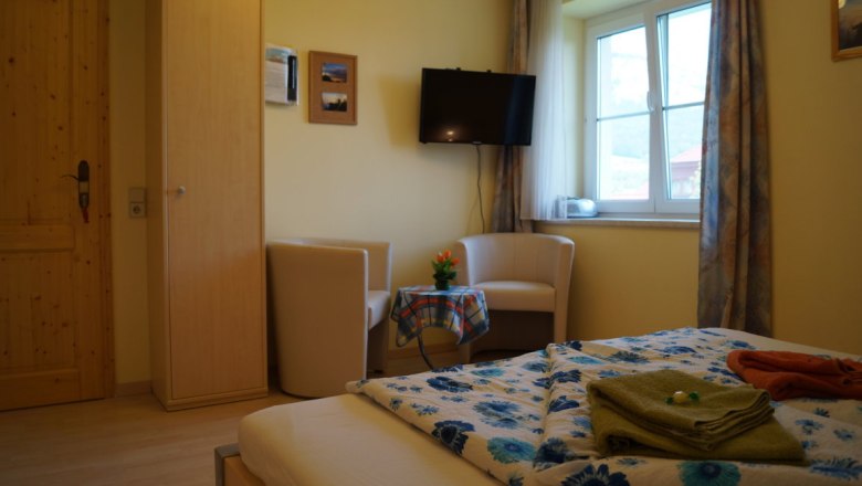 Komfortzimmer Ahorn, © Reep Komfortzimmer mit Bett, zwei Sesseln, Tisch, Fernseher und Fenster.