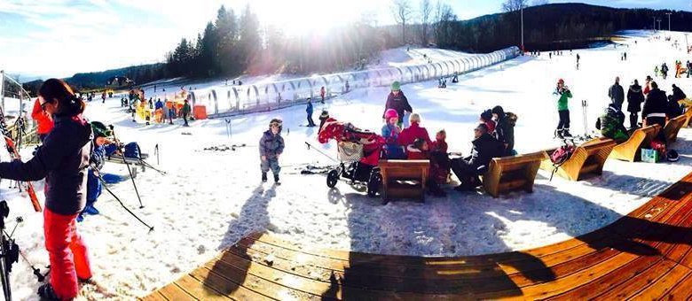 Familienskiland, © ©familienarena Winterlandschaft mit Menschen beim Skifahren und Entspannen auf Bänken im Schnee.