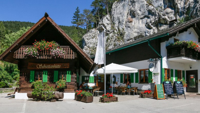 Wasserfallwirt, © Moeslinger Ein traditionelles Gasthaus mit Holzbalkon und Blumenschmuck vor einer Felswand.