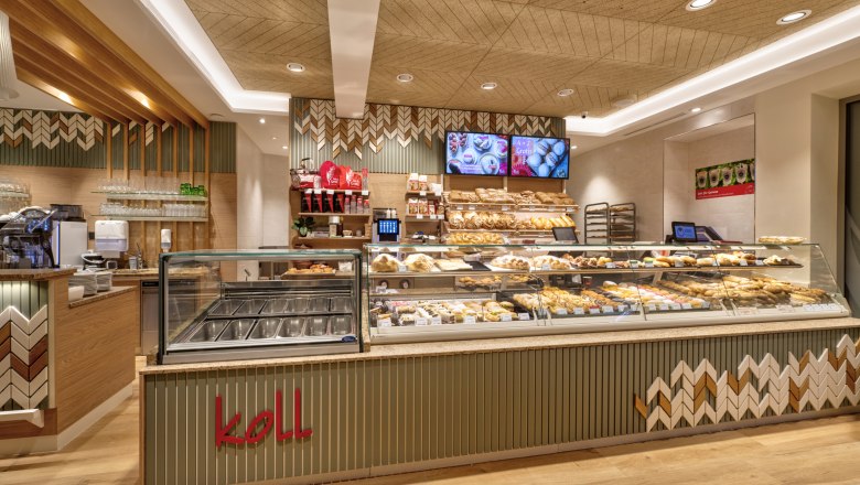 Bakery Koll, © Michaela Begsteiger, Koll GmbH Interior view of the modern bakery with counter full of baked goods and coffee machine.