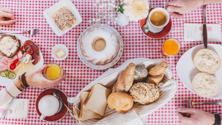 Breakfast, © Gasthof Berghof Breakfast table with bread rolls, cakes, cold cuts and drinks on a red and white checkered tablecloth.