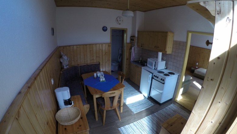 Wohnküche Ferienwohnung 1, © dmgrauszer Wohnküche in einer Ferienwohnung mit Holzmöbeln, Esstisch, Küchenzeile und Zugang zu einem Schlafzimmer.