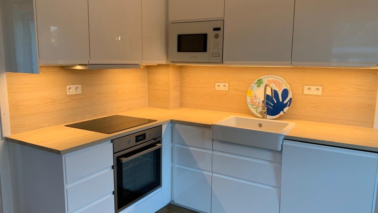 Küche, © Marianne Gschaider Moderne Küche mit weißen Schränken, Holzarbeitsplatte, eingebautem Ofen und Spüle.