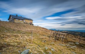 Wetterkoglerhaus am Hochwechsel, © Wiener Alpen, Christian Kremsl Berghütte auf einem Hügel mit bewölktem Himmel im Hintergrund.