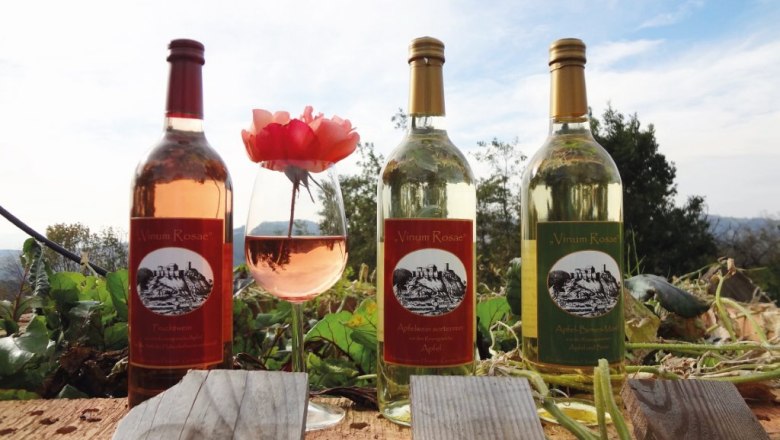 Ciders from the Winkler family, © Familie Winkler Three bottles of cider and a glass of cider with a rose on a wooden beam outside.