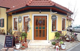 Bauernladen Stocker, © Klaus Stocker Eingang vom Bauernladen Stocker mit gelber Fassade, roten Dachziegeln und Pflanzen und Deko im Vordergrund.