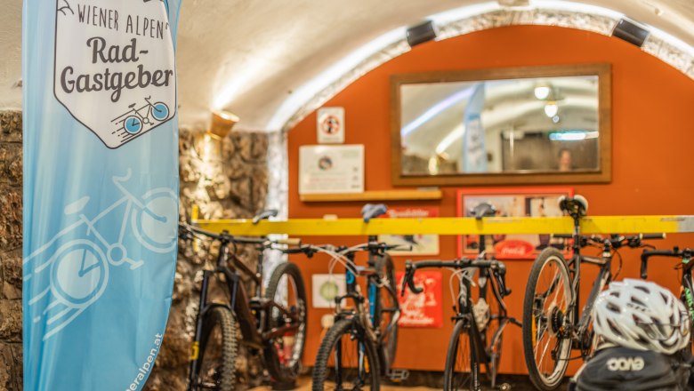 Radgarage im Landgasthof zur Schubertlinde, © Wiener Alpen/Martin Fülöp Fahrradgarage mit Fahrrädern und einem Banner der Wiener Alpen Rad-Gastgeber.