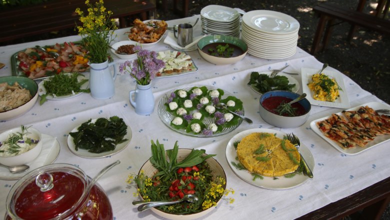 The focus is on the natural taste., © Wiener Alpen Table with white tablecloth and various dishes such as salads and cheese, next to plates and flower vases.
