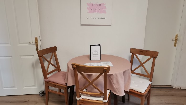 Charmantes Kaffeehaus im Herzen von Kirchberg, © Wiener Alpen Ein Tisch mit rosa Tischdecke und drei Holzstühlen in einem Café, mit einem Schild an der Wand.