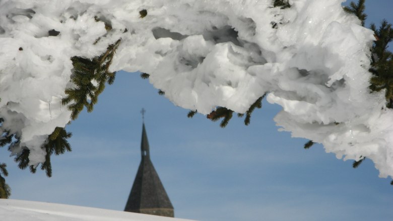 Wetterkoglerhaus, © veronika-marx-paechterin-wetterkoglerhaus Verschneiter Baum mit Kirchturm im Hintergrund.