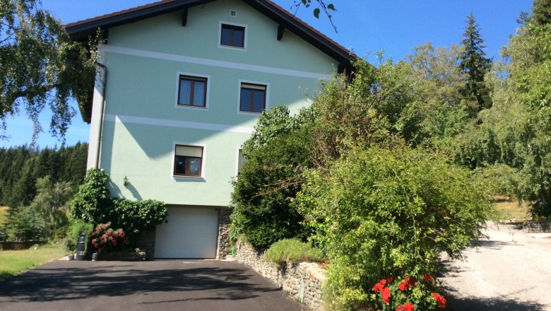 Frühstückspension Sandri, © Andreas Fischbacher Grünes Haus mit Garten und Einfahrt, umgeben von Bäumen.