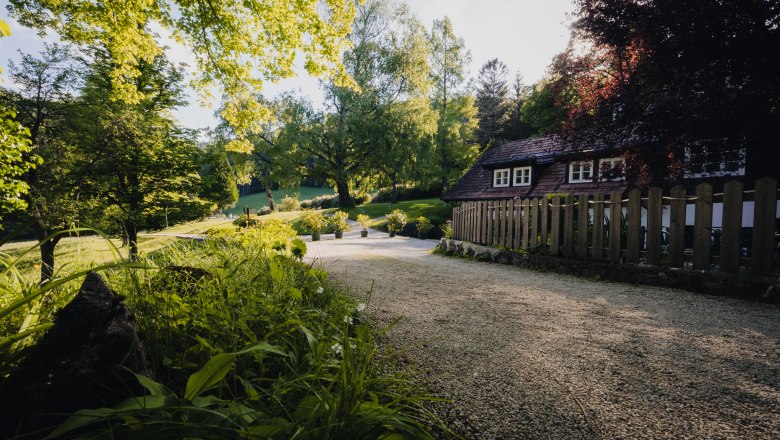 Landsitz Oberhof, © Niederösterreich Werbung / Maximilian Pawlikowsky Ein idyllischer Landsitz mit einem kleinen Haus, umgeben von Bäumen und einem Gartenweg.