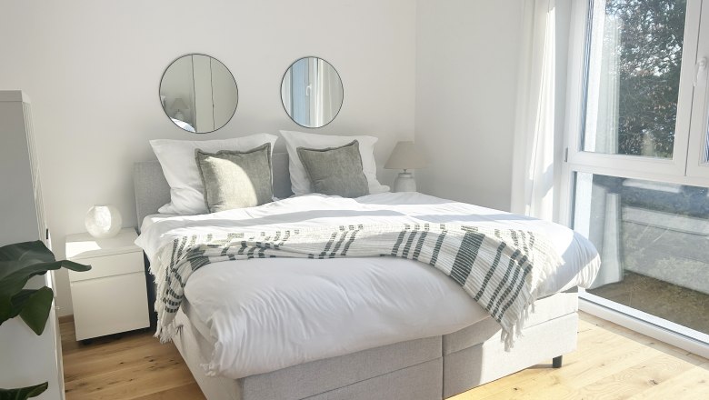 Studio, Die Feigenterrasse am Semmering, © Wiener Alpen Helles Schlafzimmer mit Doppelbett, zwei runden Spiegeln an der Wand und großen Fenstern.