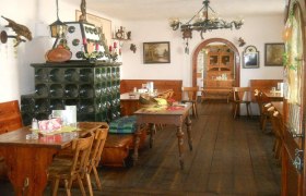 Dorfheuriger Reiterer - Loibernböck, © Thermengemeinden Innenansicht eines traditionellen österreichischen Heurigen mit Holzmöbeln und Kachelofen.