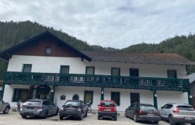 Gasthof Kreuzhof, © Wiener Alpen Ein zweistöckiges Gebäude mit grünem Balkon und geparkten Autos davor.