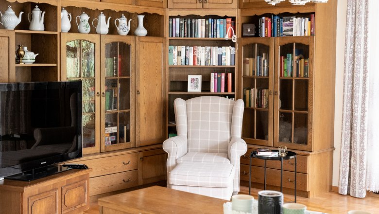 Wohnbereich Bibliothek, © Claudia Schlager Wohnzimmer mit Bücherregal, Sessel und Fernseher.