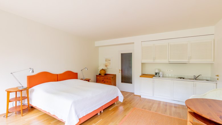 Schlafzimmer, © Wiener Alpen / Christian Kremsl Helles Schlafzimmer mit Doppelbett, Holzmöbeln und kleiner Küchenzeile.