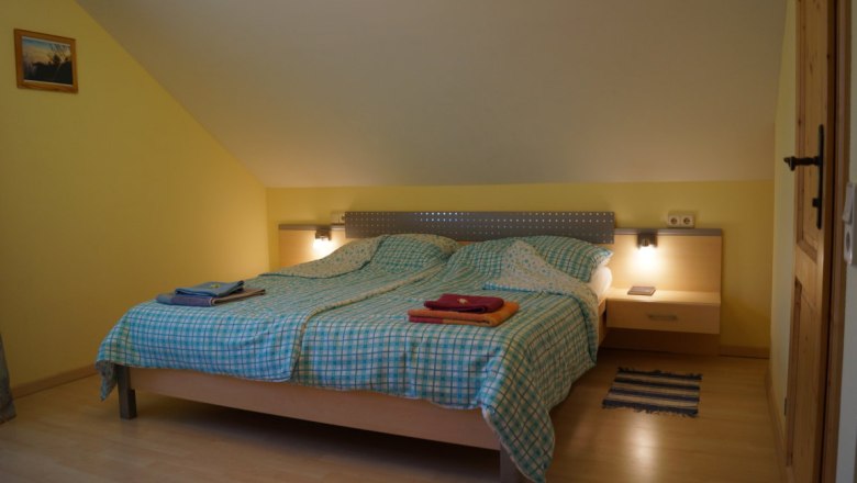 Ahornzimmer, © Reep Ein gemütliches Schlafzimmer mit einem Doppelbett, gelben Wänden und einem kleinen Nachttisch mit Lampe.