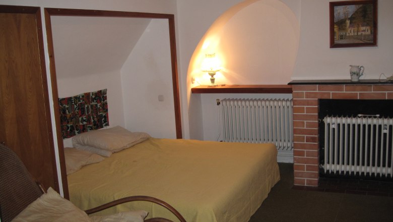 Schlafzimmer, © Stein Ein gemütliches Schlafzimmer mit einem Bett, einem Sessel, einer Lampe und einem Kamin.