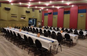 Tafel im Saal, © Markus Kiener Ein großer Saal mit langen, gedeckten Tischen und schwarzen Stühlen, bereit für ein Event.