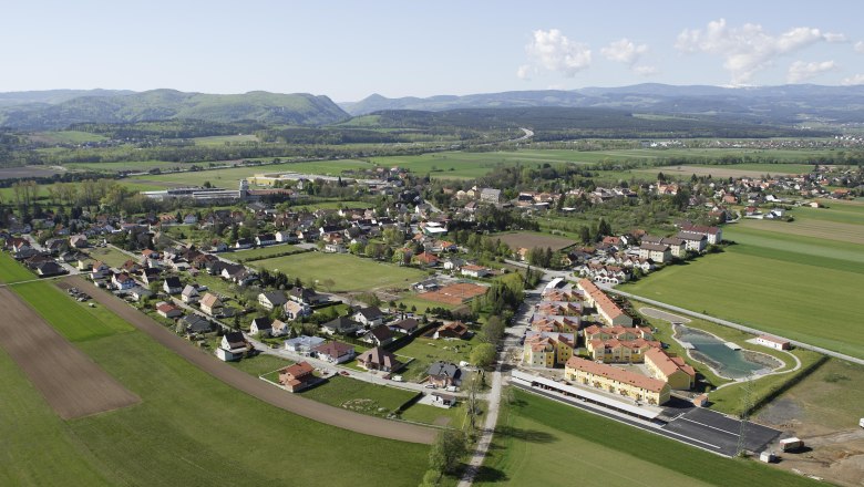 Breitenau, © Gemeinde Breitenau Luftaufnahme eines Dorfes mit Feldern und Hügeln im Hintergrund.