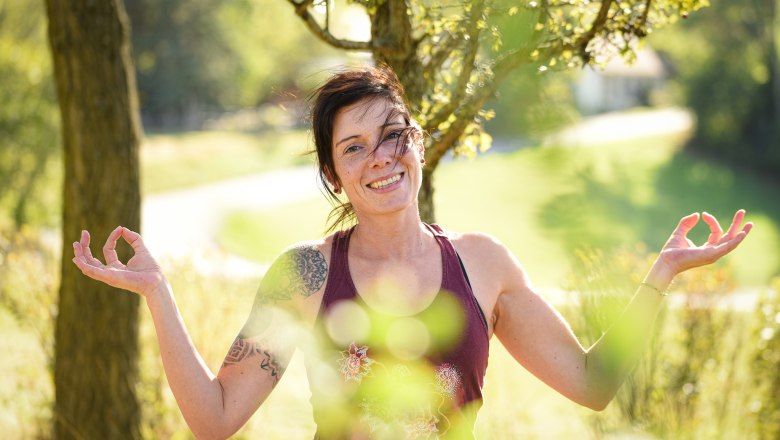 Praxis mit Leidenschaft, © Yoga.imEinklang Frau in Yoga-Pose im Freien, lächelnd vor einem Baum.