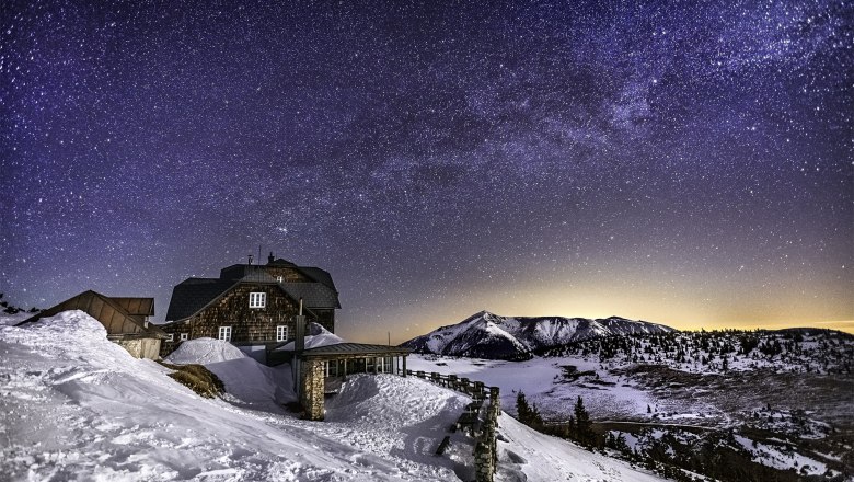 Bei der Schneeschuhwanderung kommt man am Ottohaus vorbei., © Wiener Alpen/Kremsl Sternenklare Nacht über einer verschneiten Berghütte und Berglandschaft.
