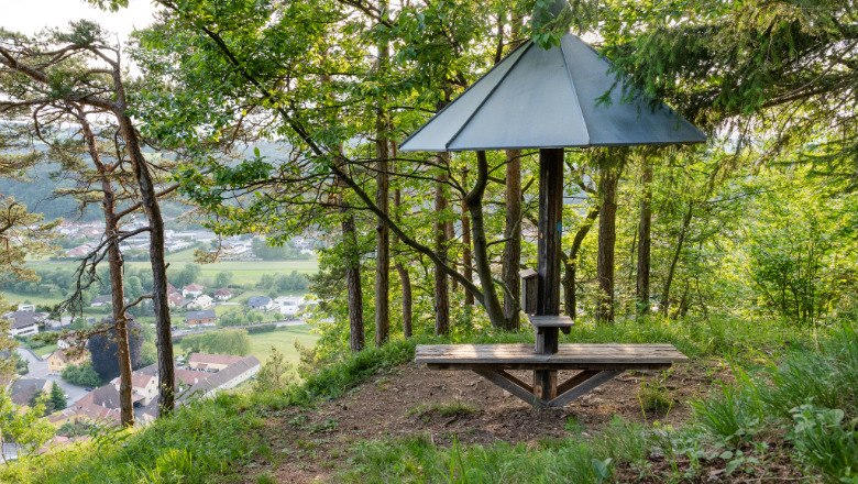 Viewpoint, © Claudia Schlager A viewpoint with a bench and roof, surrounded by trees, with a view of a valley and houses.