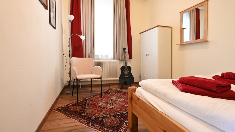 Kleines Zimmer, © Christine Kuppelwieser Kleines Zimmer mit Bett, Teppich, Stuhl, Stehlampe, Gitarre und Schrank.