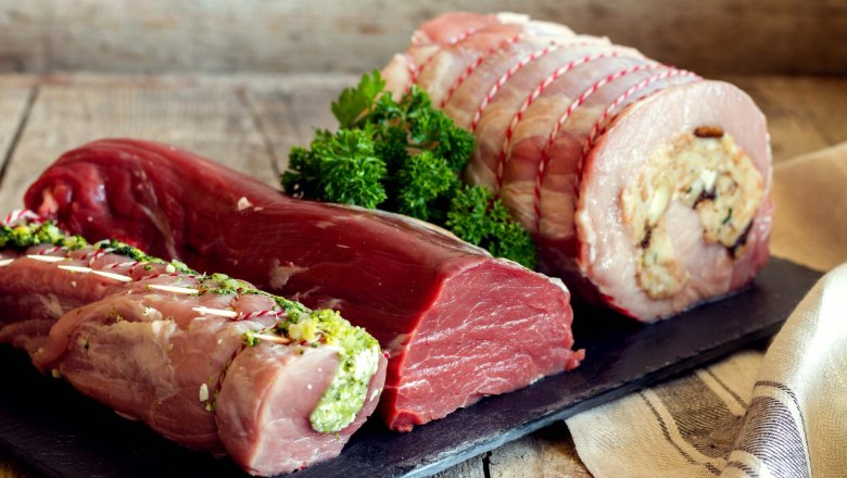 Fleischspezialitäten, © Sooo gut schmeckt / Viktoria Kornfeld Verschiedene Fleischstücke auf einem Holzbrett, dekoriert mit Kräutern.